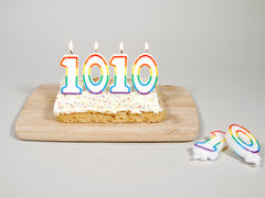 A photo of a cake with four candles in the shape of the digits 1010. The candles are lit, and two more candles are nearby