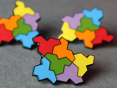 Photo of three of the pin on a table; the pin is made up of six hat-shaped tiles arranged together, in red, orange, yellow, green, blue and purple