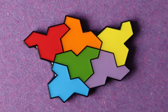 Photo of a single pin attached to some purple material; the pin is made up of six hat-shaped tiles arranged together, in red, orange, yellow, green, blue and purple
