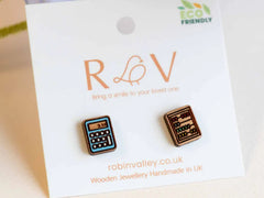 Photo of the 'abacus calculator' style earrings, which are both made from rounded rectangular pieces of wood, one etched with a calculator hand painted light blue showing '3.154' on the screen, and the other showing an abacus with red, blue, green and yellow beads on four horizontal bars. They are on a mounting card with the Robin Valley logo.