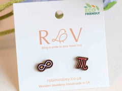 Photo of the 'Pi Infinity' style earrings, which are a red pi symbol and a pale purple infinity symbol, made from laser cut wood. They are on a mounted card with the Robin Valley logo, and next to a nice flower. Aww.