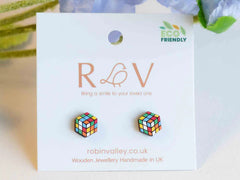 Photo of Rubik's cube earrings, which are flat wooden hexagons printed with a scrambled Rubik's cube design. They are on a mounted card with the Robin Valley logo, and next to a nice flower. Aww.