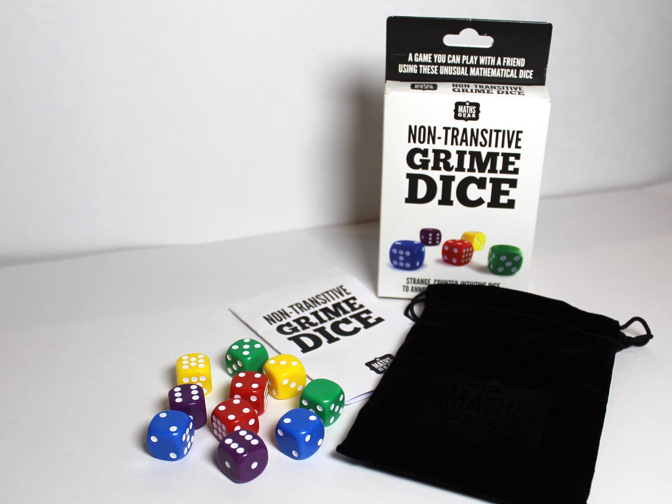 Photo of a box of Non-Transitive Grime Dice, in front of which is a set of 10 dice, a fabric bag and an instruction leaflet. Text on the box reads "A game you can play with a friend using these unusual mathematical dice"