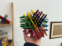 A photo of the rod packing structure made using these pencils, held up in Matt's hand. In the background you can see a simpler structure just made from the red/green/blue pencils; also in shot is a framed piece of brown paper from the Numberphile video about the Parker square, and a jar of dice.