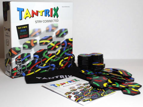 Photo of the game box, in front of which are a pile of hexagonal tiles covered in red/green/yellow/blue curved lines, a booklet labelled Tantrix Activity Guide, and a fabric bag with the word Tantrix printed on it