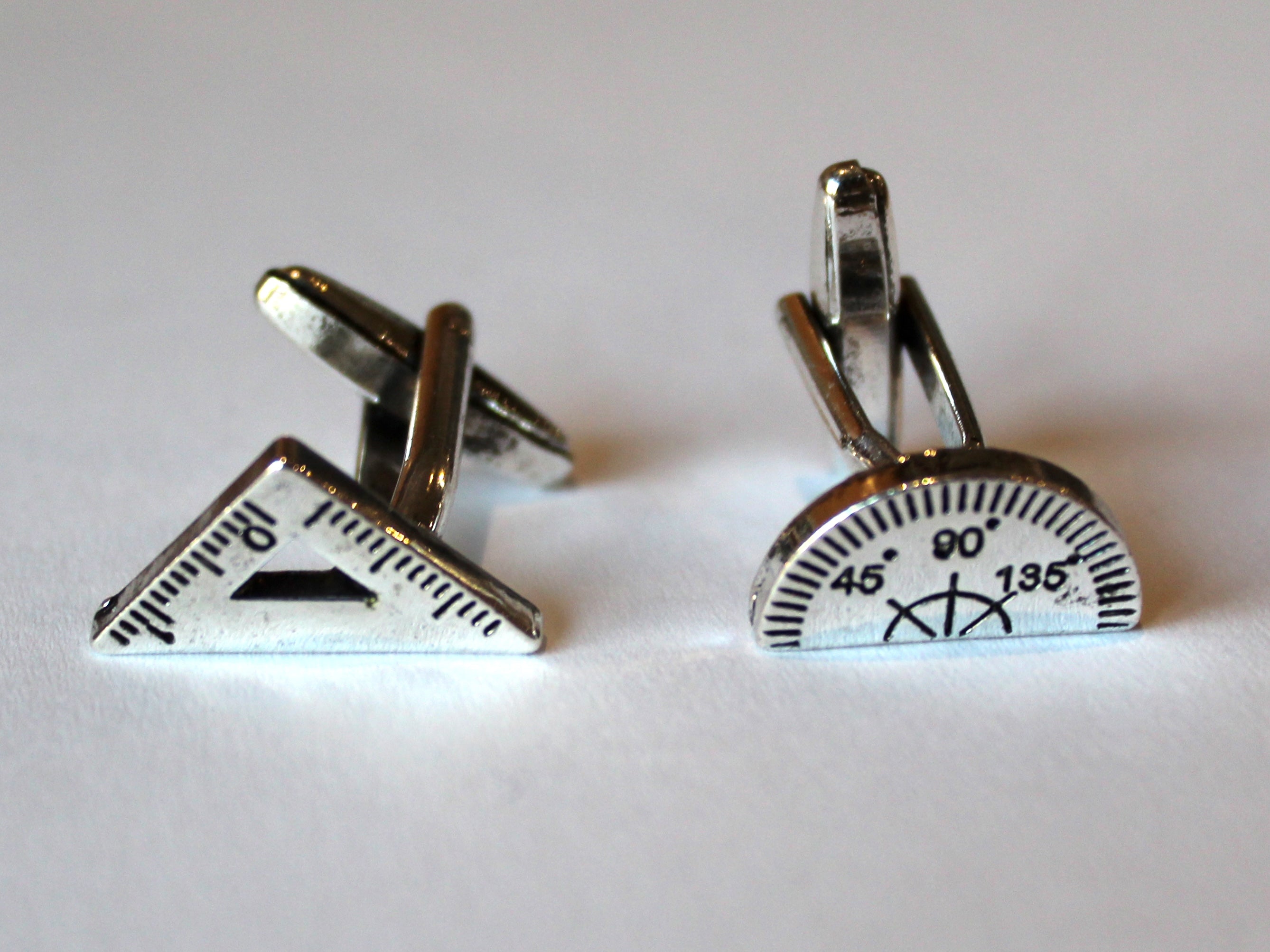 Photo of the pair of cufflinks, which are a metal set square and protractor