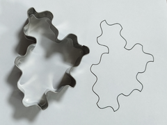 Metal cookie cutter in the shape of a spectre tile on a white sheet of paper with a traced outline next to it.