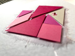 Photo of the pink tangram card from a low angle, showing that the pieces are raised slightly from the front of the card.