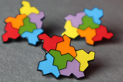 Photo of three of the pin on a table; the pin is made up of six hat-shaped tiles arranged together, in red, orange, yellow, green, blue and purple